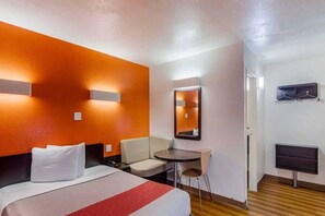A hotel room with a bed, a desk, a chair, a mirror, and a television.