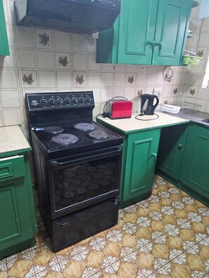 Eine Küche mit einem schwarzen Herd, grünen Schränken, einem roten Toaster und Fliesen mit Muster.