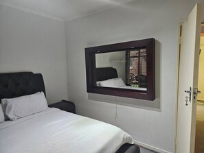Une chambre d’hôtel avec un lit, une table de chevet, un miroir et une porte.