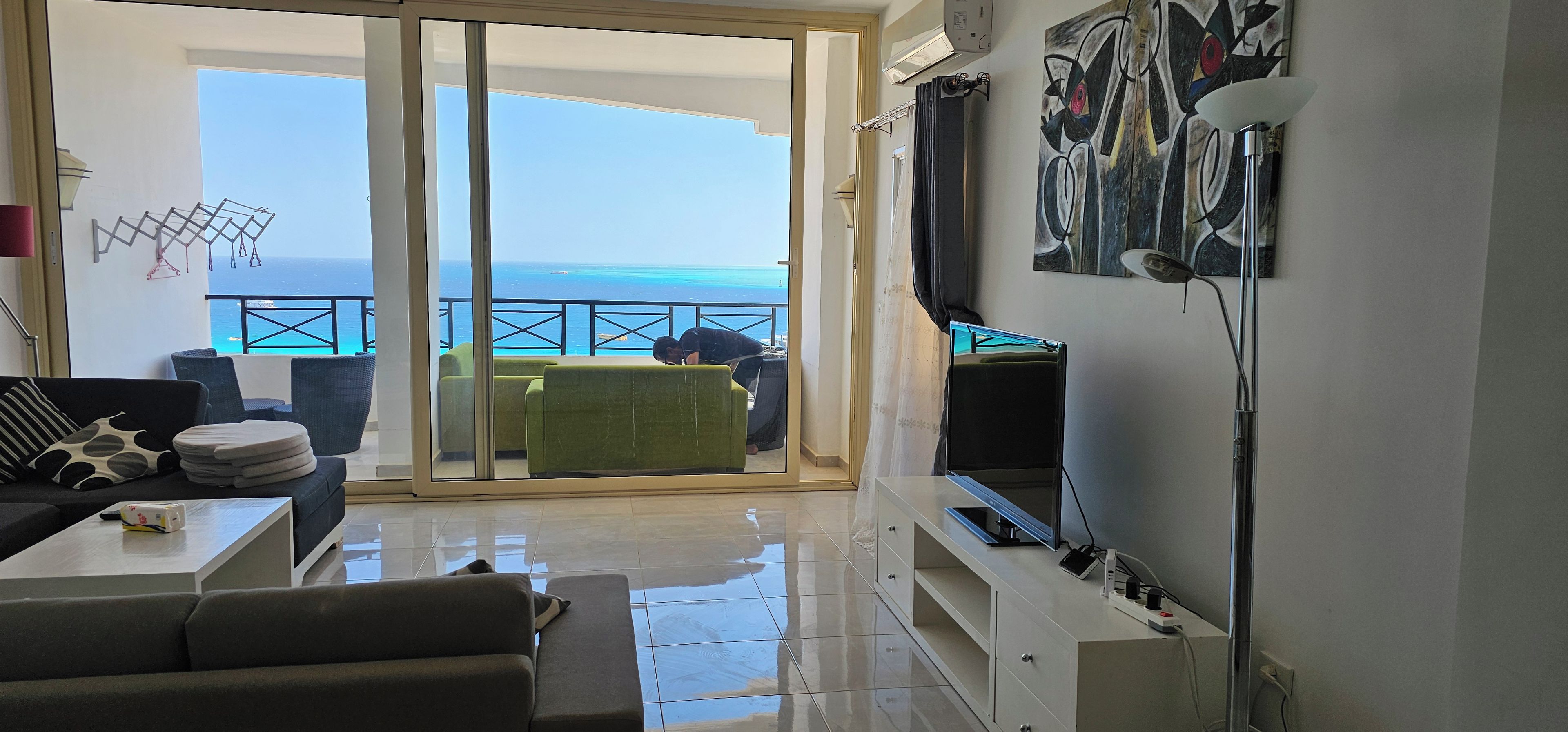 Een woonkamer met uitzicht op de oceaan, een balkon met een stoel en een televisie aan de muur.