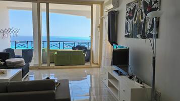Een woonkamer met uitzicht op de oceaan, een balkon met een stoel en een televisie aan de muur.