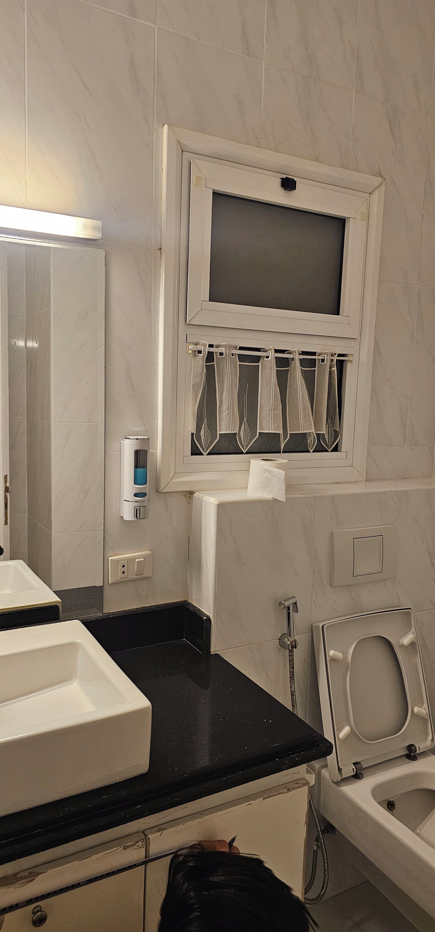 Een badkamer met een wit wastafelmeubel, een spiegel, toilet en een raam met gordijnen.