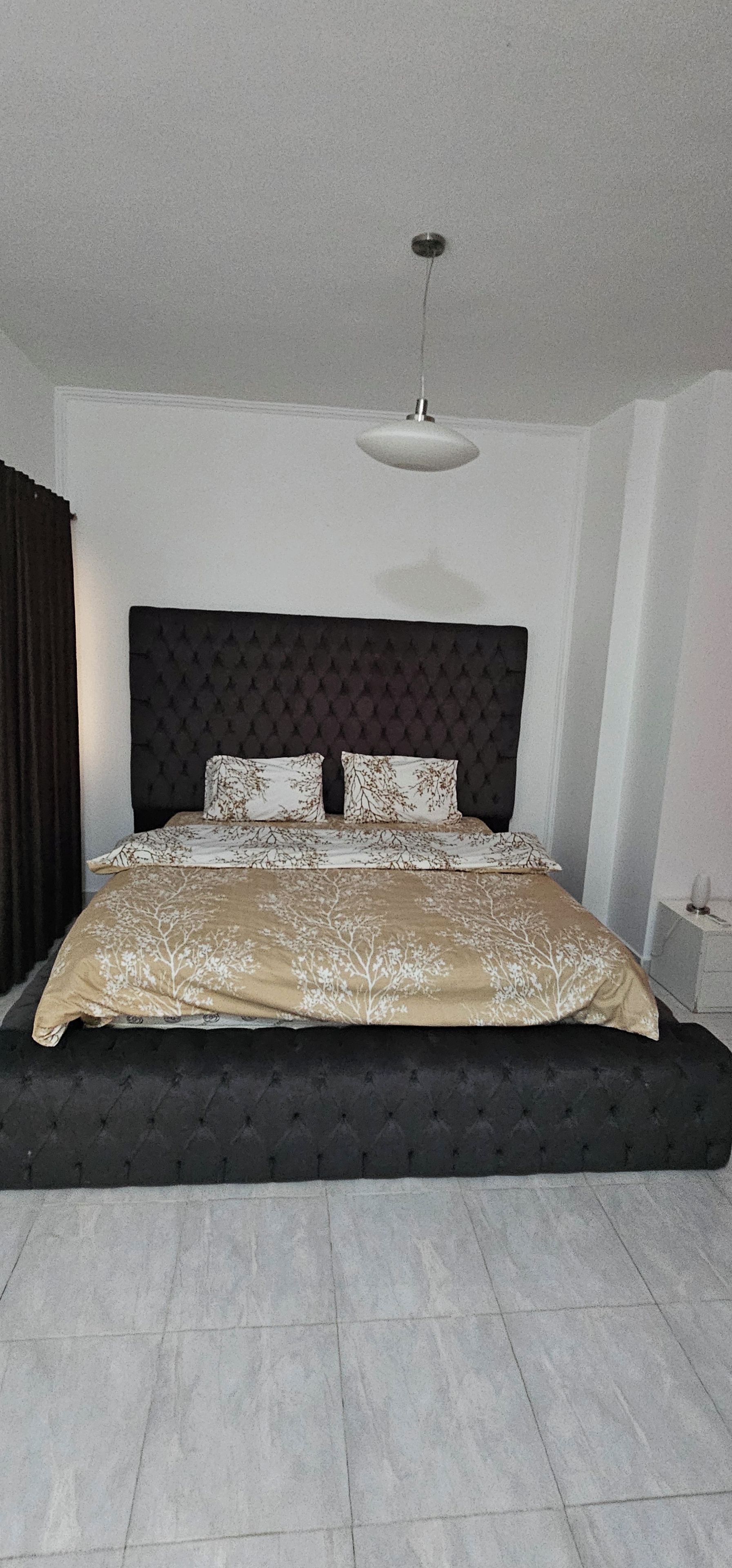 Een slaapkamer met een groot bed, een donkere hoofdbord en een hanglamp.