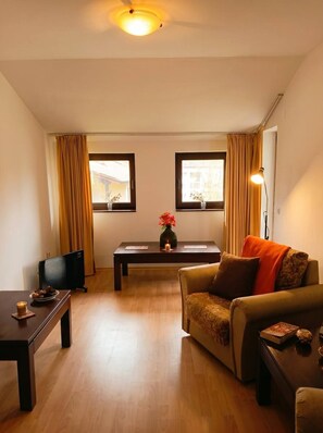 Ein Wohnzimmer mit einer Couch, einem Couchtisch, einem Fernseher und zwei mit Vorhängen versehenen Fenstern.