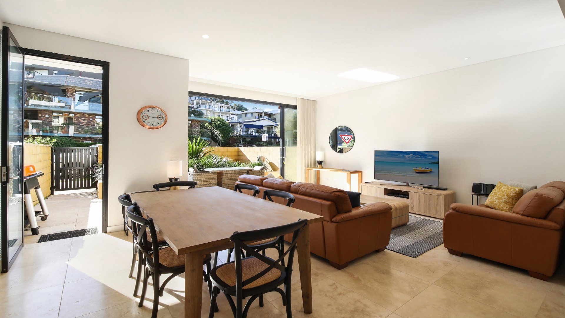 A modern living room with a dining area, a sofa set, a TV, and a view through a glass door.