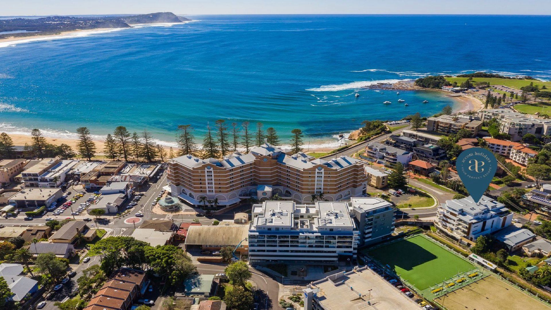 An aerial view of a coastal hotel with multiple buildings, a parking lot, and a beach.
