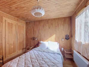 A wooden-paneled room with a bed, a hanging light fixture, a small table, and a radiator. - Chalet Pelou - 7 peoples - Morzine (Morzine)