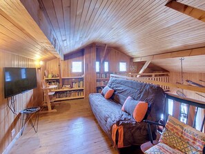 A cozy cabin interior with a wooden ceiling, a sofa with cushions, a television, and bookshelves. - Chalet Pelou - 7 peoples - Morzine (Morzine)