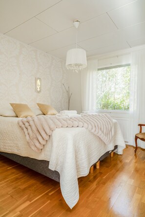 Een slaapkamer met een groot bed, een kroonluchter, een raam met gordijnen en een houten vloer.