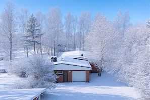 Een besneeuwd woongebied met een gelijkvloers bakstenen huis, een garage, en een helderblauwe lucht.