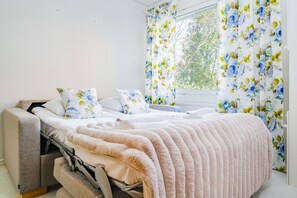A bedroom with a bed, pillows, a blanket, a window with curtains, and a view of trees outside. - River View Family Home By Lapland Host (Rovaniemi)