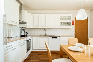 A modern kitchen with white cabinetry, a wooden countertop, a dishwasher, and a dining area with a wooden table and chairs. - River View Family Home By Lapland Host (Rovaniemi)