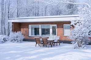 A brick building with a patio table and chairs, surrounded by snow-covered trees. - River View Family Home By Lapland Host (Rovaniemi)