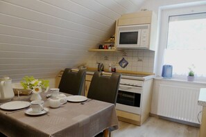 Eine Küche mit Esstisch für zwei Personen, einer Mikrowelle und einem Fenster mit Pflanze.