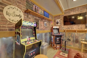 A room with arcade games, a TV, and a 'Welcome' sign on the wall. - Harbour View - Lake Cabin w/ Game Room & Fire Pit (Odessa)
