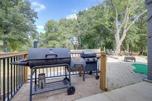 An outdoor patio with a barbecue grill and a grill cart, surrounded by a wooden deck and trees. - Harbour View - Lake Cabin w/ Game Room & Fire Pit (Odessa)