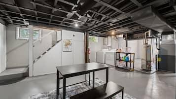 A basement with a table, bench, washing machine, and a shelf with cleaning supplies.