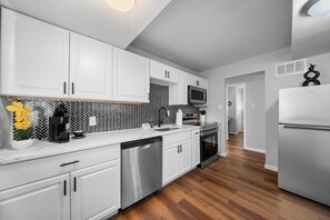 A modern kitchen with white cabinets, a black and white herringbone backsplash, stainless steel appliances, and a wooden floor. - Home sweet home (St. Louis)