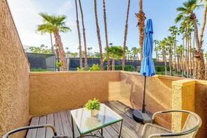 A patio with a glass table, wicker chairs, a blue umbrella, and tall palm trees in the background. - Sip, Soak & Stargaze: Palm Desert Retreat! (Palm Desert)