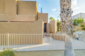 A building with a textured facade, a white metal fence, and a palm tree. - Sip, Soak & Stargaze: Palm Desert Retreat! (Palm Desert)