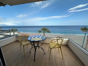 Un balcon avec vue sur la plage, comprenant une table ronde et deux chaises.