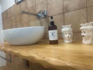 A bathroom with a large white basin, a bottle of hand wash soap, and two decorative ceramic figures on the countertop. - Blue Wave Apartment: Relax by the Sea, Panoramic Terrace, and Modern Design (Letojanni)