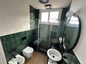 Un bany modern amb dutxa de vidre, vàter blanc i un lavabo.