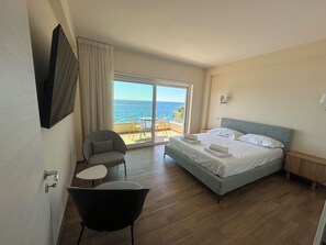 Une chambre d’hôtel avec un lit, une chaise, une petite table, une télévision et une vue sur l’océan.