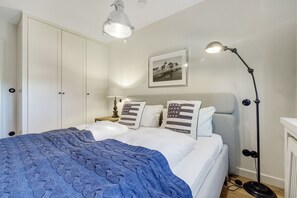 Een netjes opgemaakt bed met een blauwe deken, een bedlampje en twee kussens met een Amerikaans vlagontwerp.