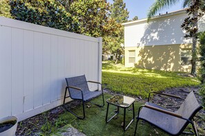 A backyard with a white fence, two chairs, a small table, and a house in the background. - Family Townhome Near Disney | Pool | Gated (Kissimmee)