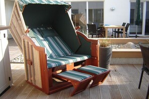 Ein Korbsessel mit gestreiften Kissen auf einer Terrassenfläche.