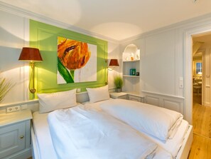 A hotel room with a large bed, two bedside lamps, a green accent wall, and a painting of a flower. - Holiday Apartment Oystercatcher (Kampen)
