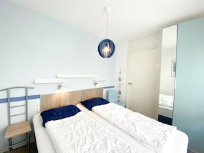 A bedroom with a bed, bedside tables, a hanging light fixture, and a door. - We05 Holiday Home With Outdoor Pool (Westkapelle)