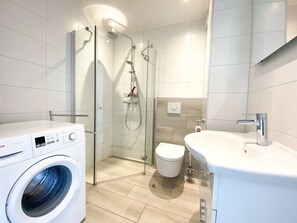 A modern bathroom with a glass-enclosed shower, a toilet, a sink, and a washing machine. - We05 Holiday Home With Outdoor Pool (Westkapelle)
