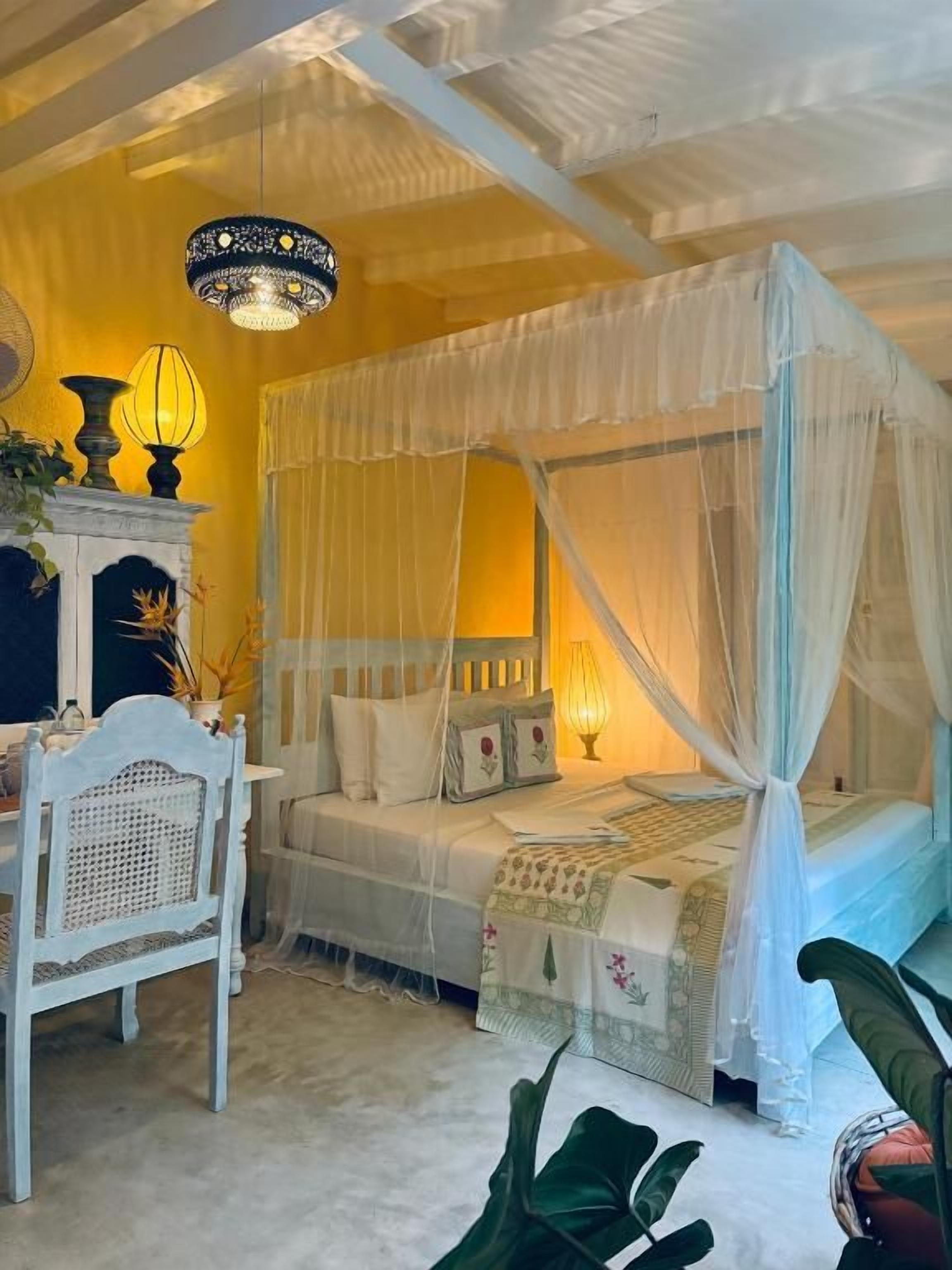 A bedroom with a canopy bed, bedside lamps, a chair, and a table with decorative items.