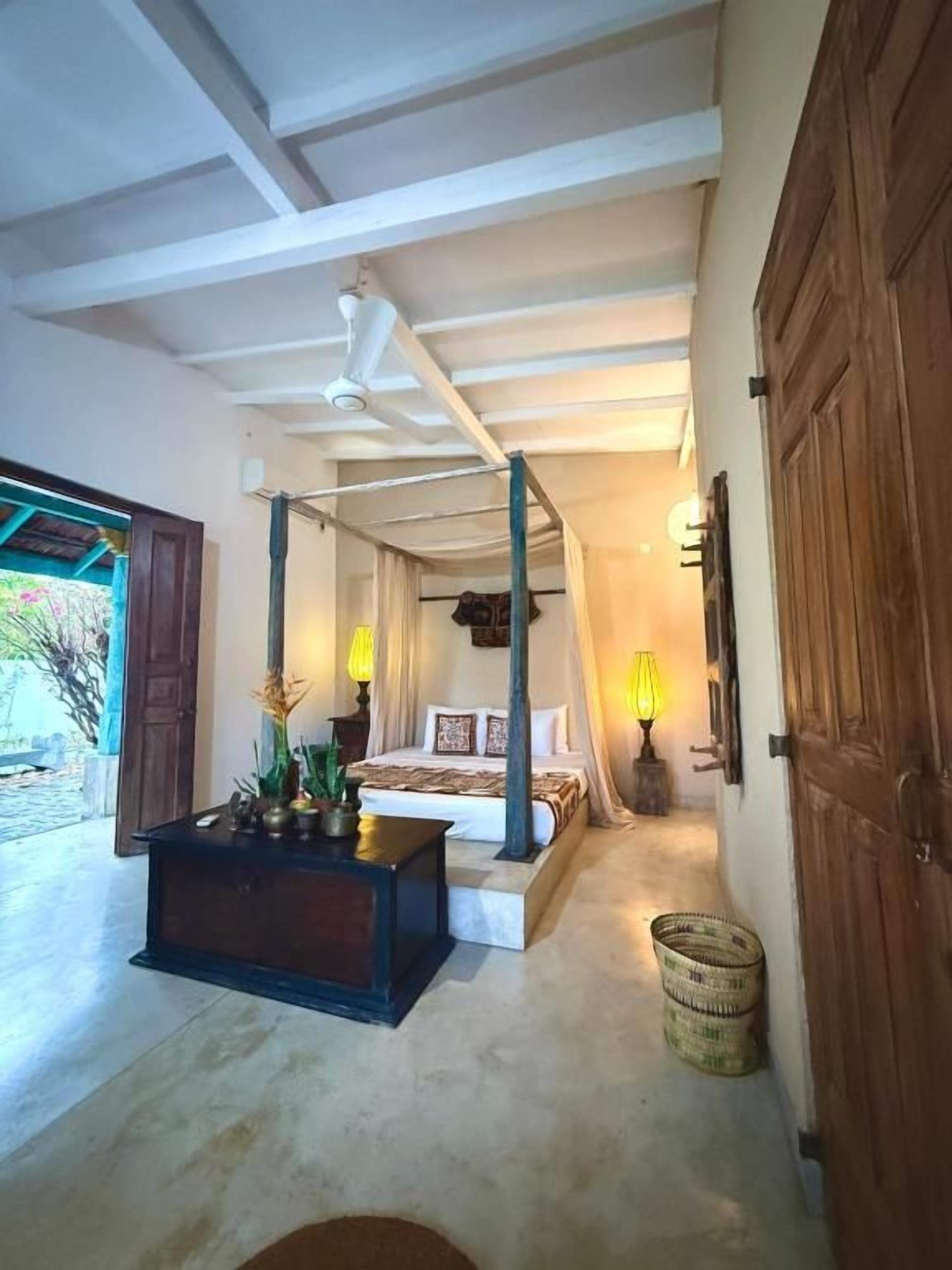 Een slaapkamer met een hemelbed, nachtkastje en een lamp.
