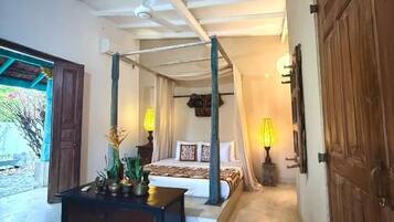 Een slaapkamer met een hemelbed, nachtkastje en een lamp.