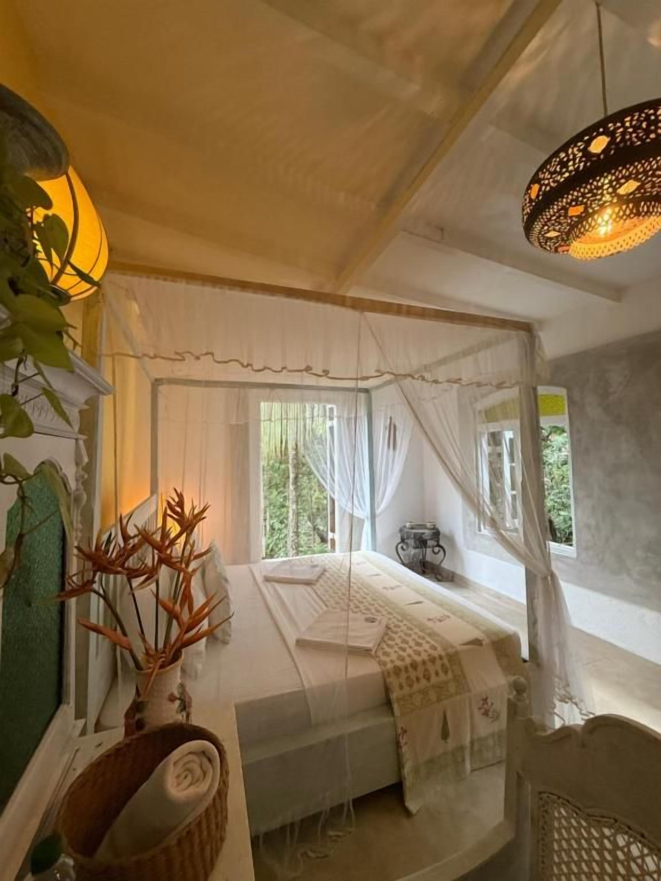 Un dormitorio con cama a dosel, una mesita de noche, una lámpara y una ventana con cortinas.