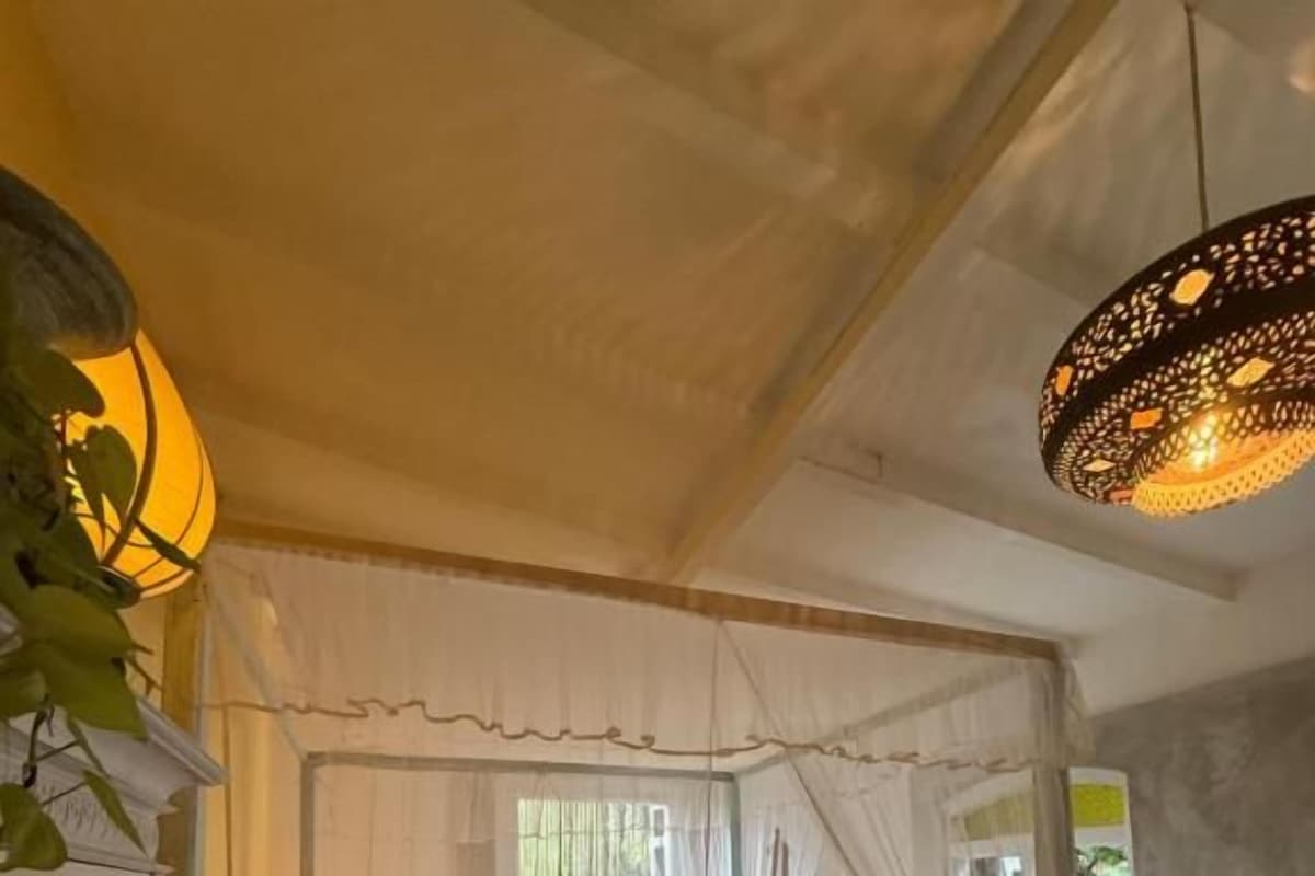 Un dormitorio con cama a dosel, una mesita de noche, una lámpara y una ventana con cortinas.