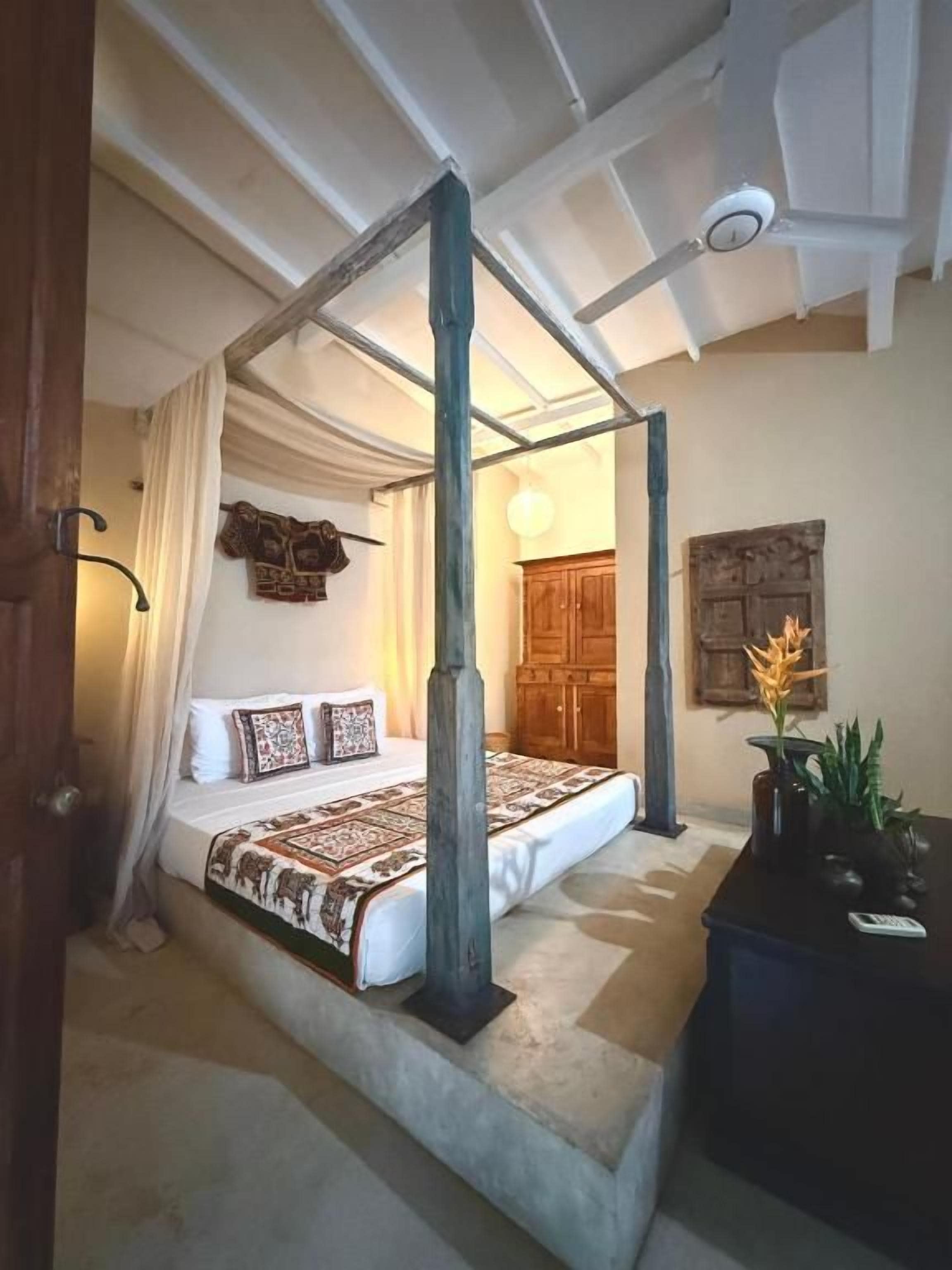 Un dormitorio con una cama con dosel, un armario de madera y una mesita con una planta.