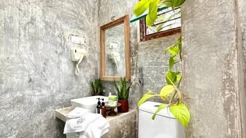 A bathroom with a concrete wall, a white toilet, a sink with a mirror, and a plant.