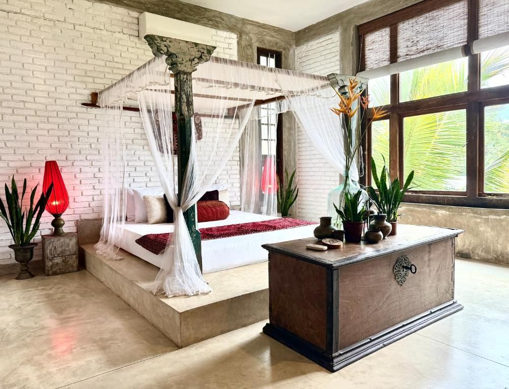 A bedroom with a four-poster bed, a wooden nightstand, and a large window with a view of greenery.