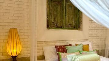 A bedroom with a bed, a lamp, a window with curtains, and a brick wall.
