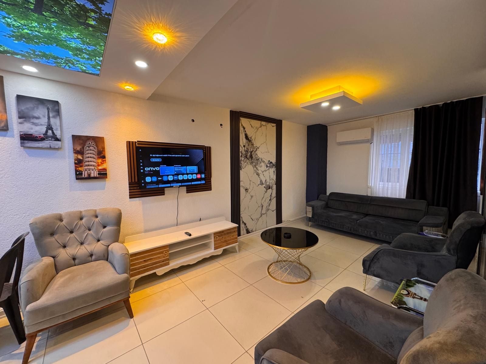 A modern living room with a flat-screen TV mounted on the wall, a sofa, a coffee table, and a chair.