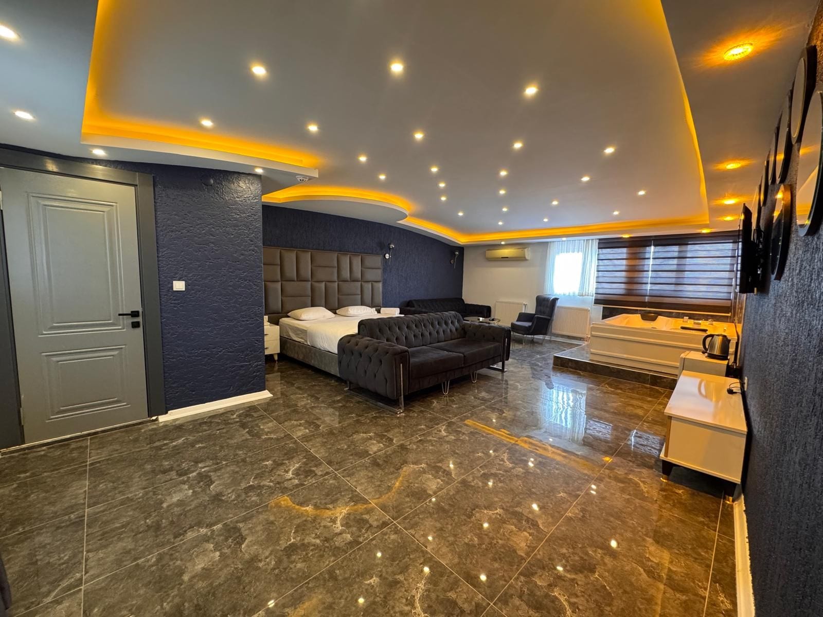 A modern bedroom with a large bed, a sofa, a seating area, and a bathtub.