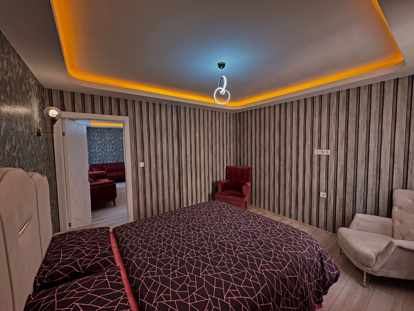 A modern bedroom with a bed, two chairs, and a ceiling light fixture.