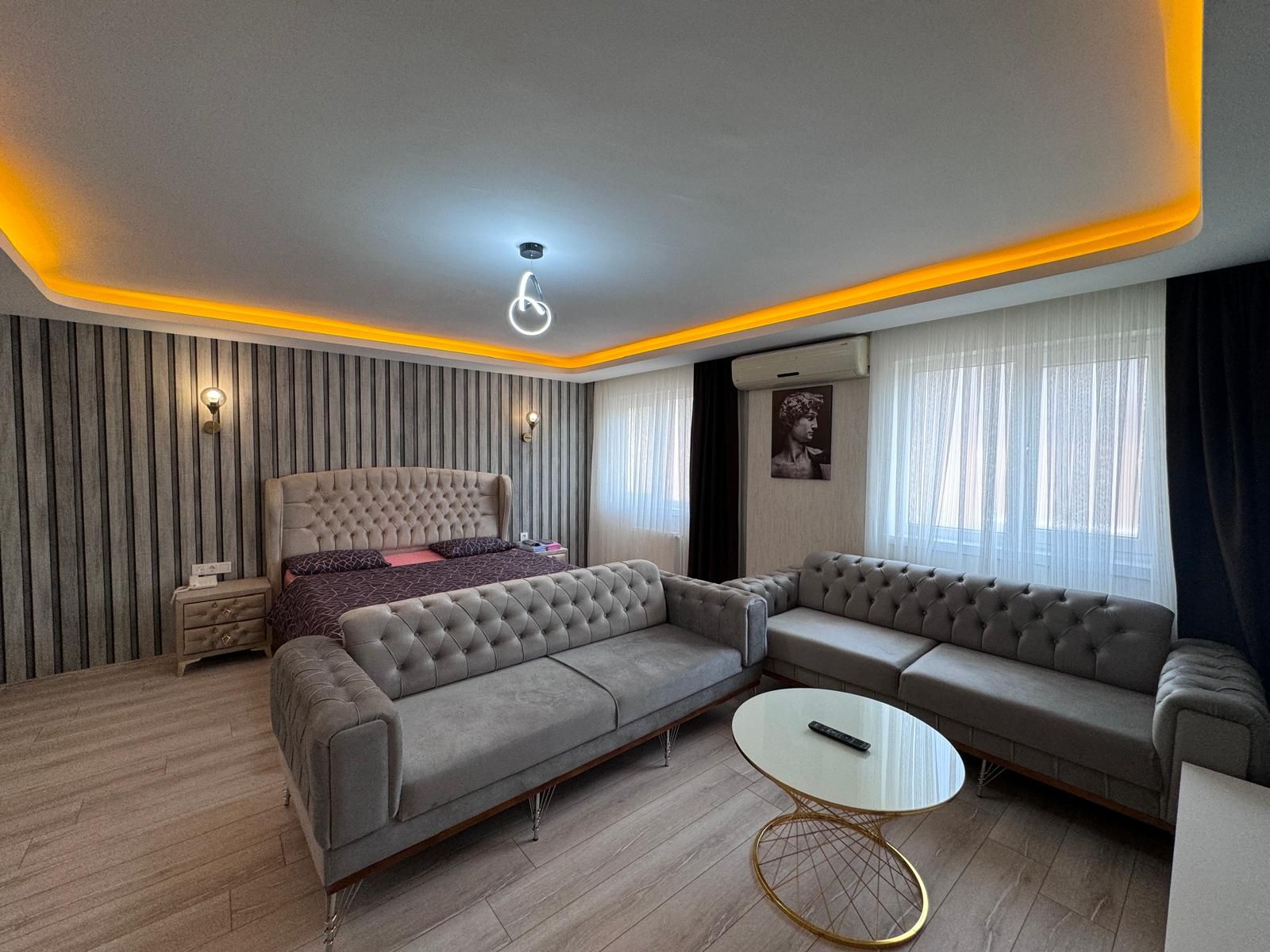 Una sala moderna con sofá, una mesita redonda y una cama con cabecera.