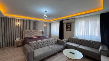 Una sala moderna con sofá, una mesita redonda y una cama con cabecera.