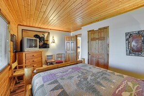 Ein Zimmer mit Holzboden, einem Bett, einem Schrank, einem Sessel, einem Fernseher und einer Tür.