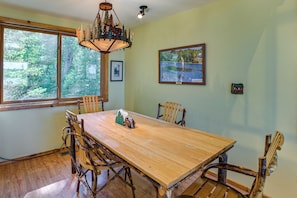 A dining area with a wooden table and chairs, a chandelier, and framed pictures on the walls. - Upscale Beachfront Log Home on Lake Huron Shores (Drummond)